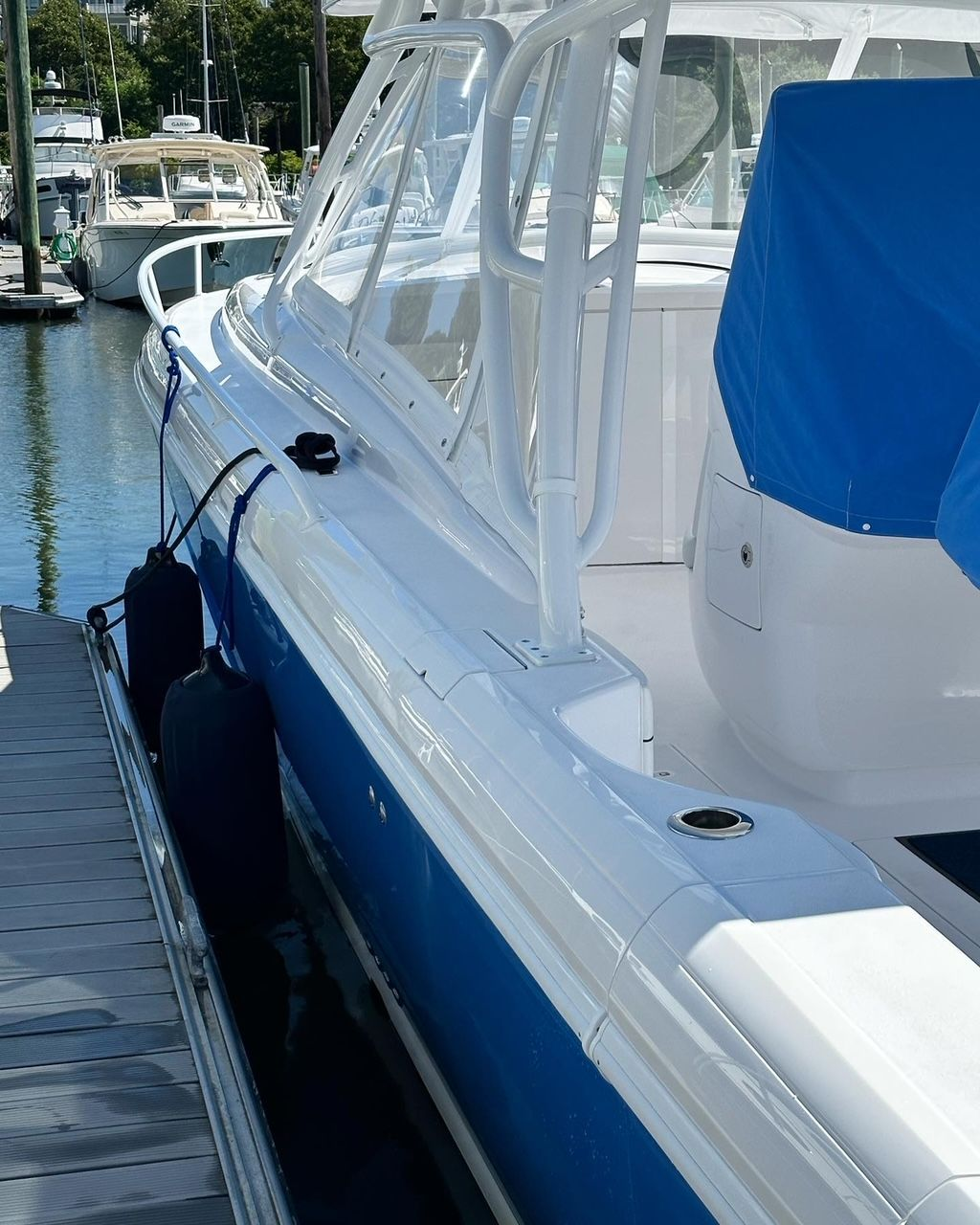 White and blue boat docked at a marina with covered seating and protective bumpers.