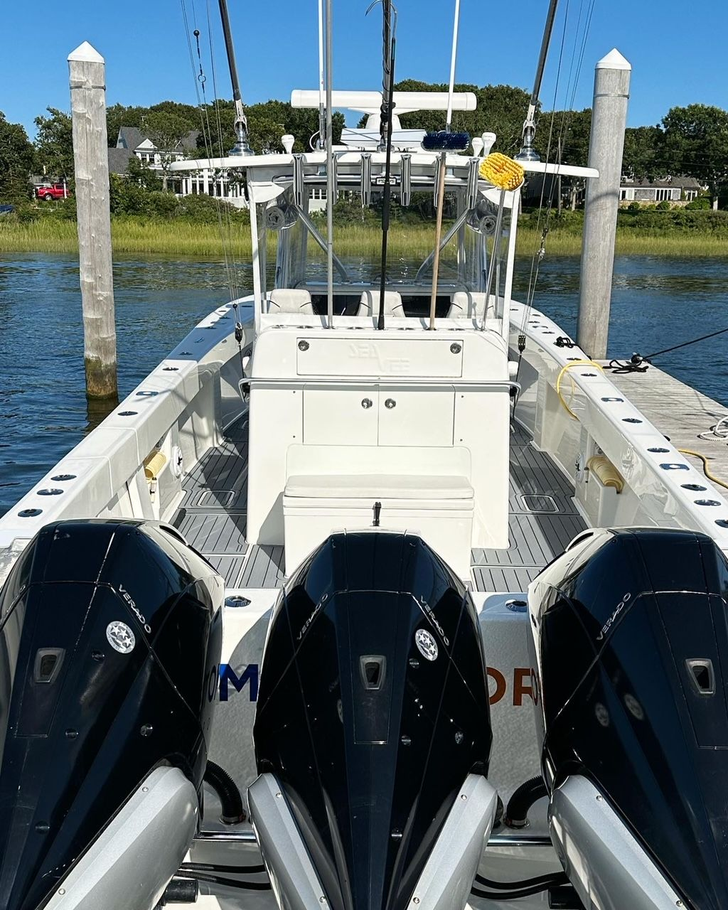 White boat with triple black outboard motors docked, blue water, sunny day.
