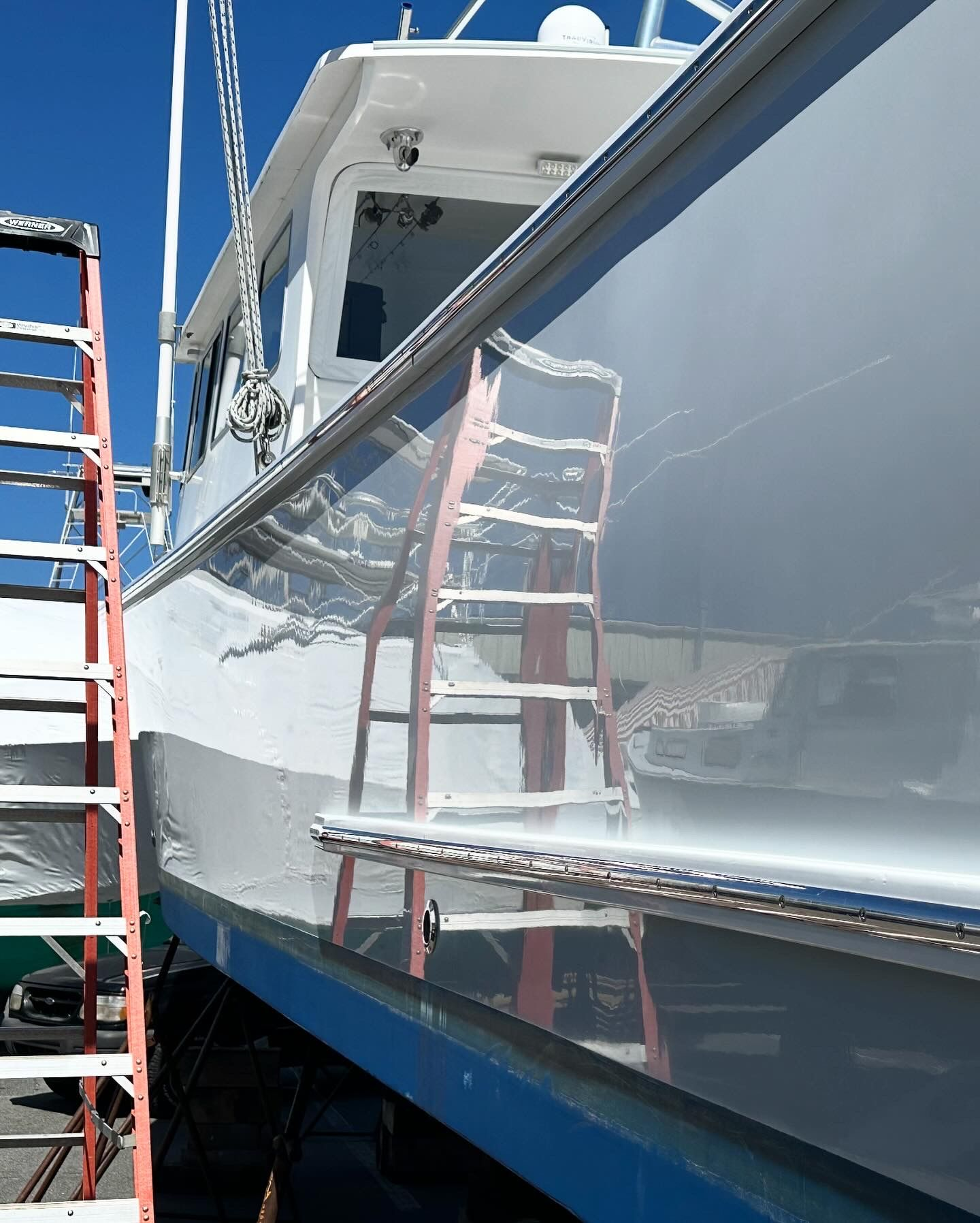 Shiny boat with a ladder leaned against its side, under a clear blue sky.