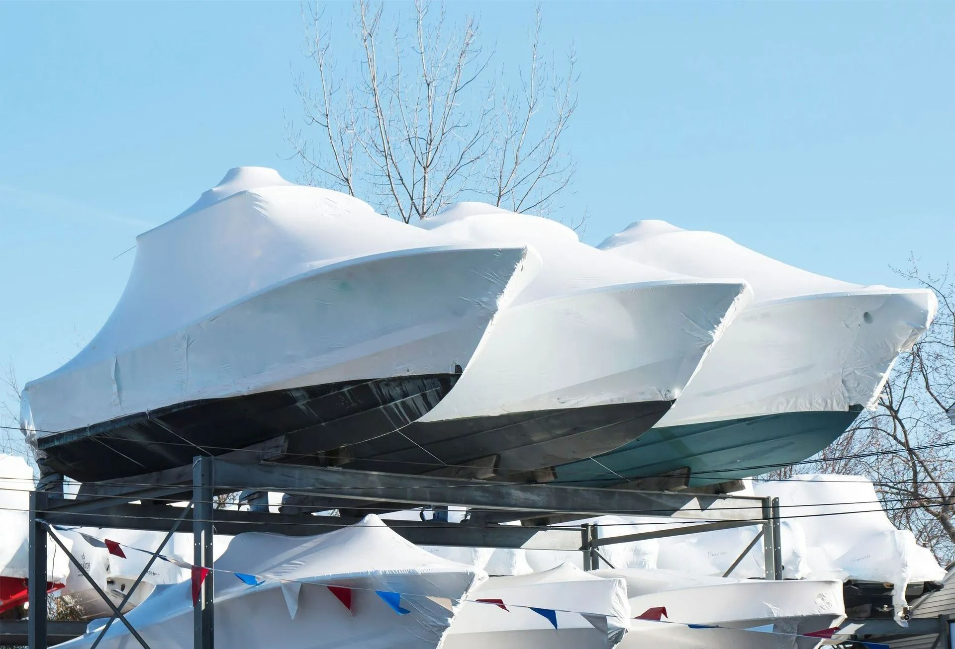 Boats covered in white tarps stacked on metal racks, outdoors.