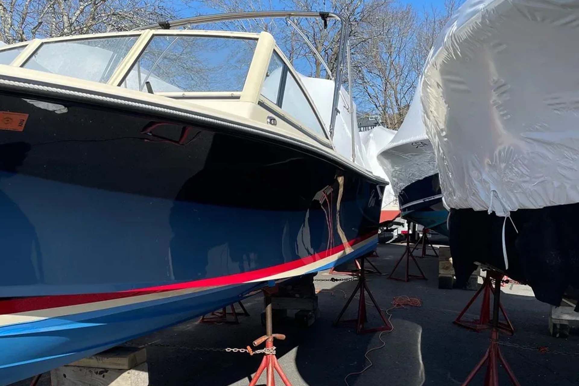 A dark blue boat with a cream-colored windshield frame, propped on metal stands in a storage lot.