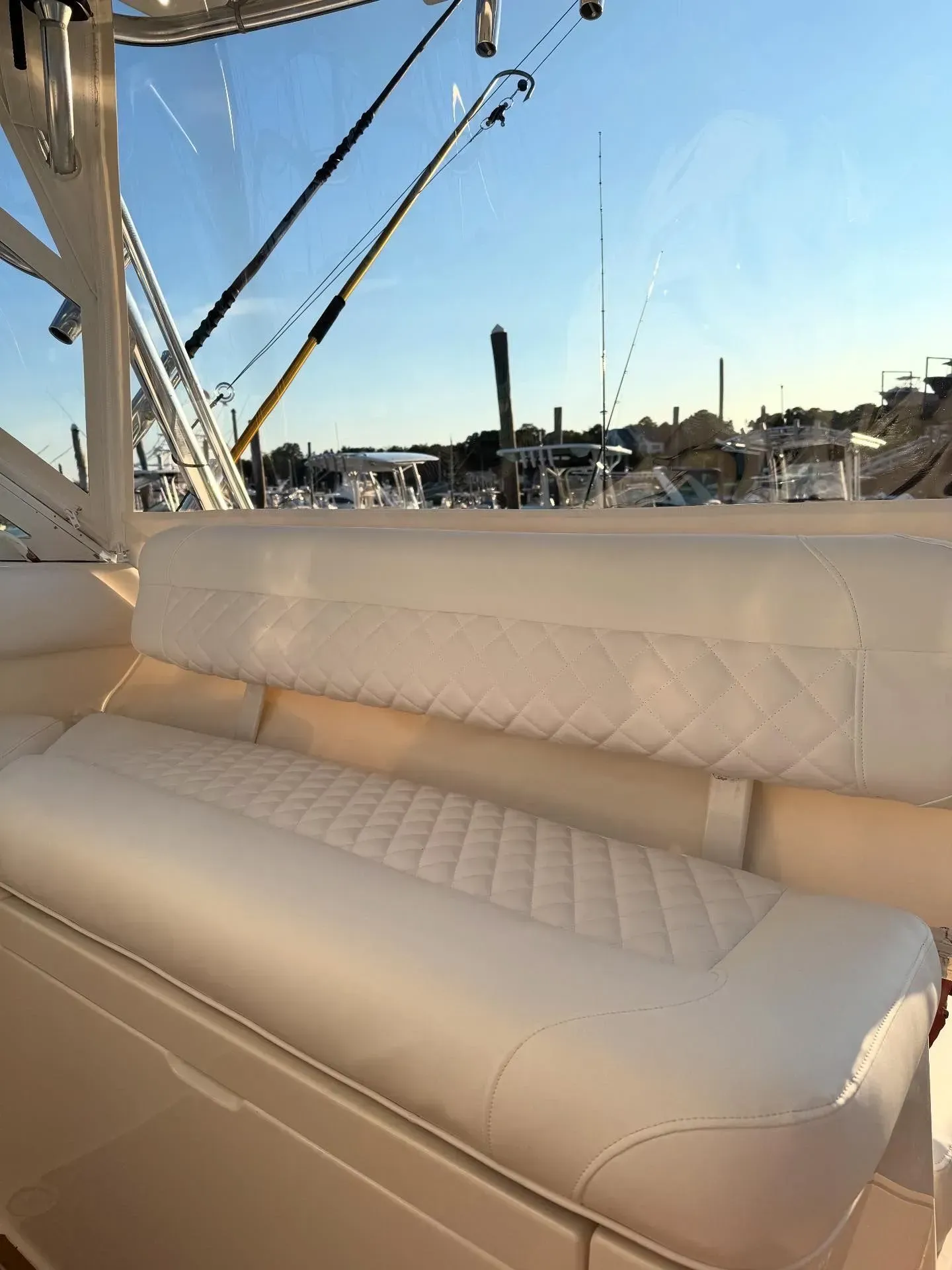 A white boat bench with diamond stitching, fishing rods overhead, and a harbor in the background.