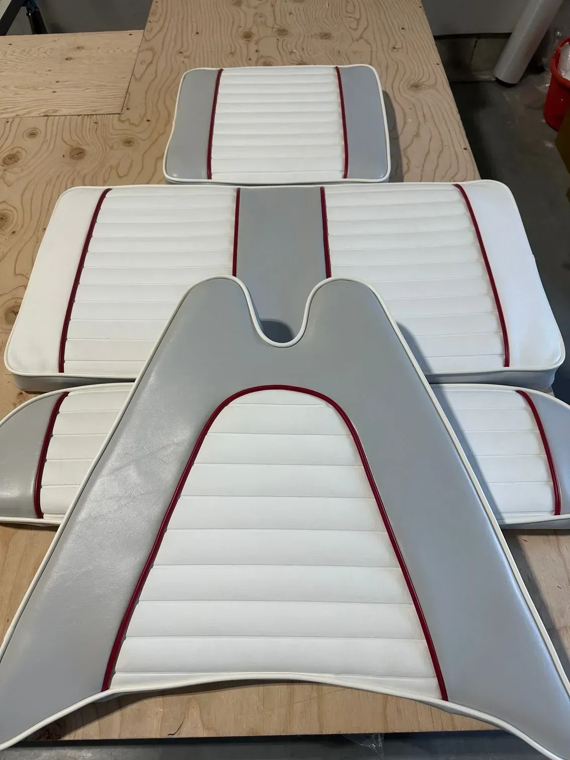 Boat seat cushions in white and gray with red piping, arranged on a wooden surface.