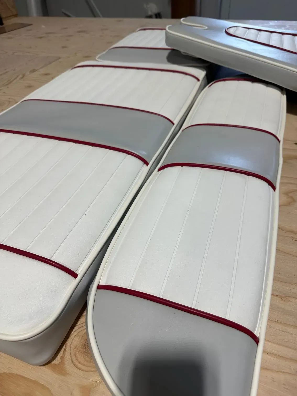 White and gray boat seats with red trim, angled on a wooden surface.