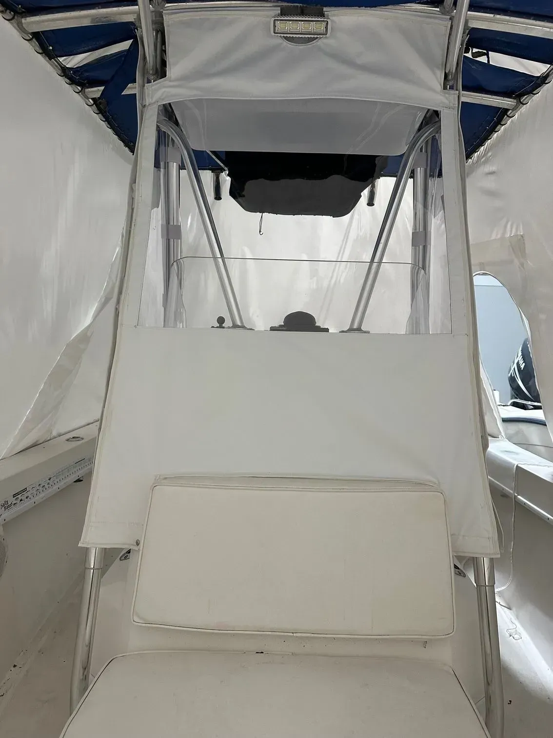 Interior view of a boat helm with white canvas panels, clear plastic windows, and a cushioned seat.