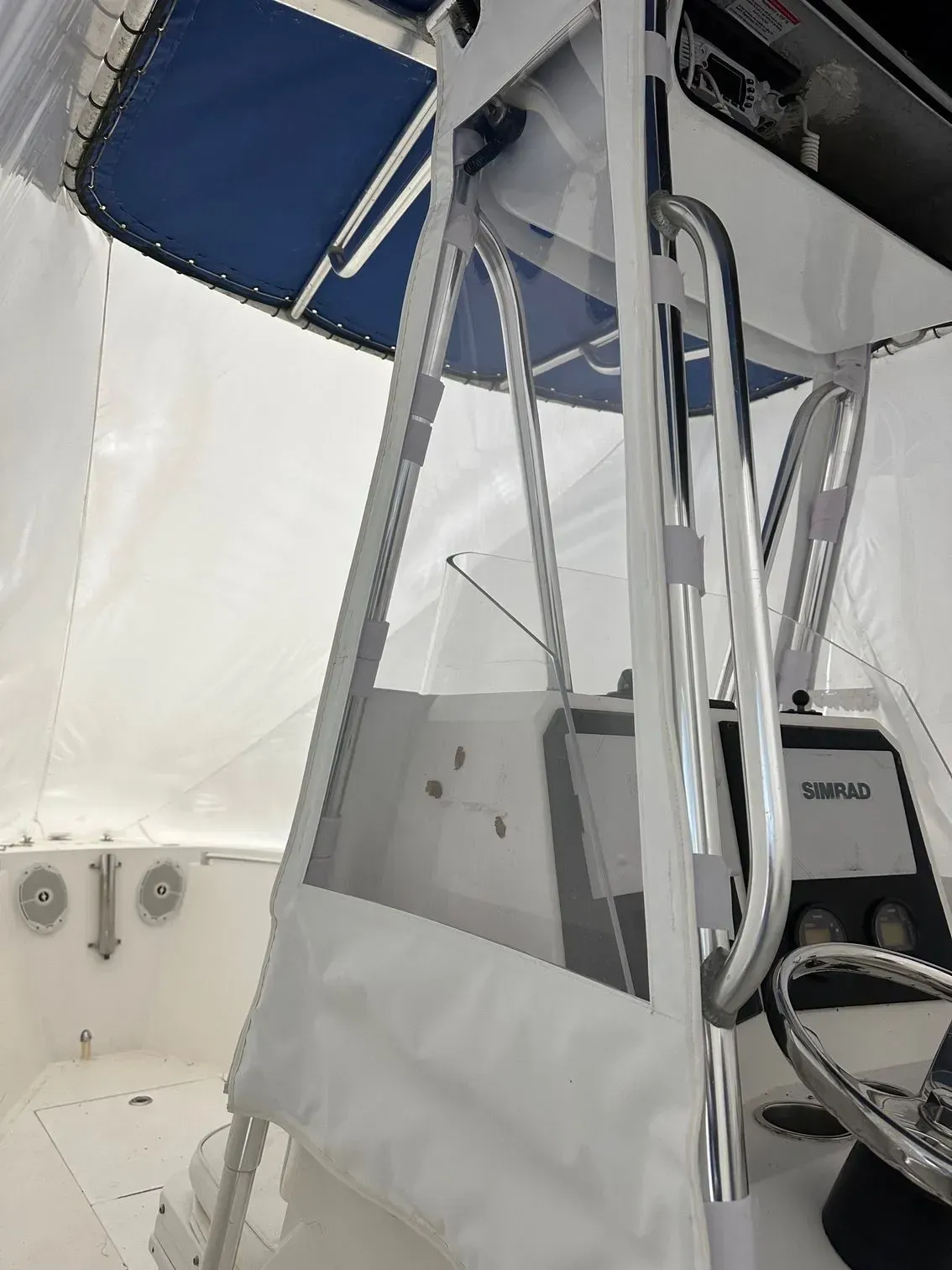 Interior of a boat with clear vinyl panels, a steering wheel, and a blue canopy.