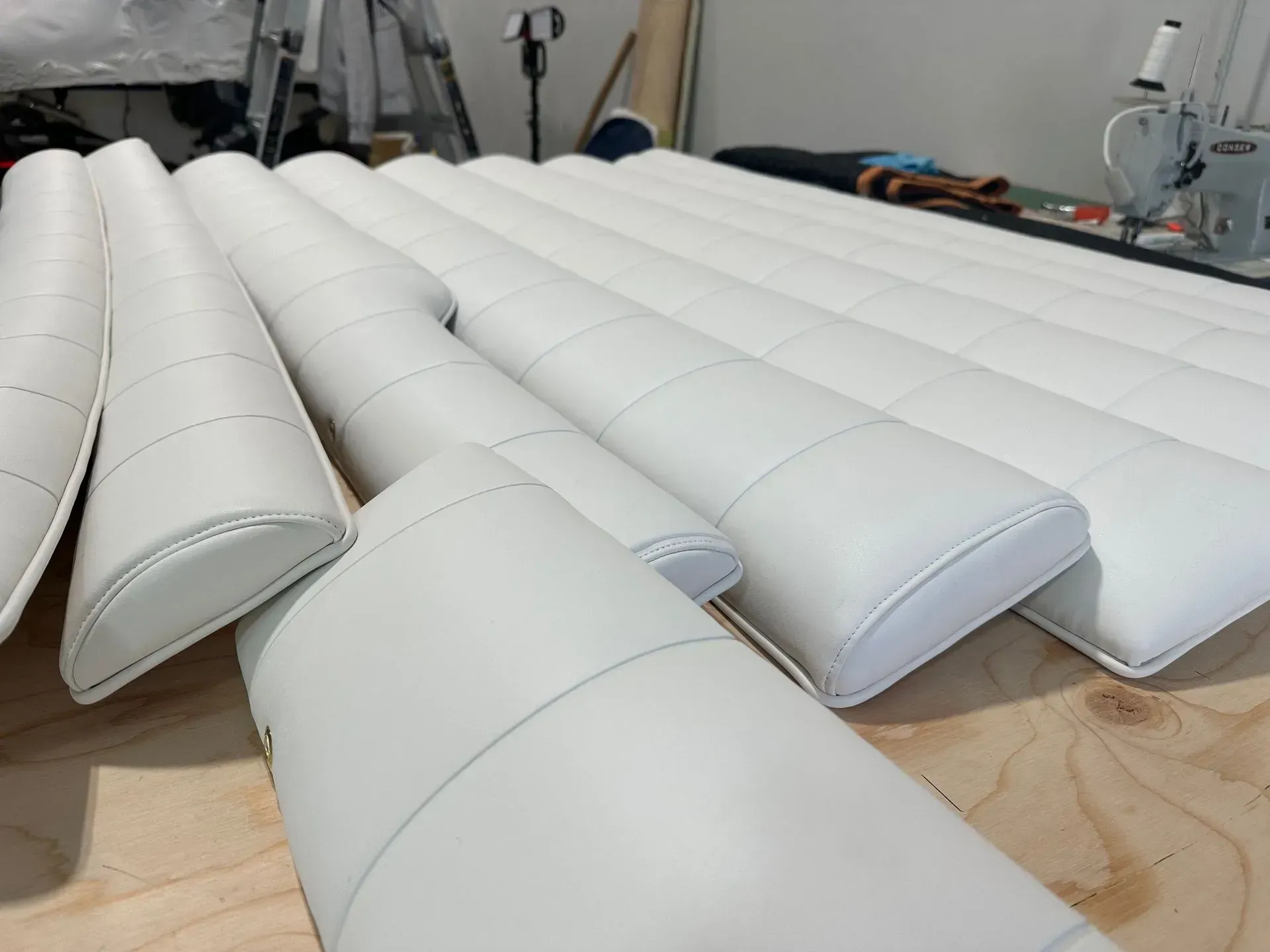 White upholstered tubes arranged on a wooden surface, with a sewing machine and workshop background.
