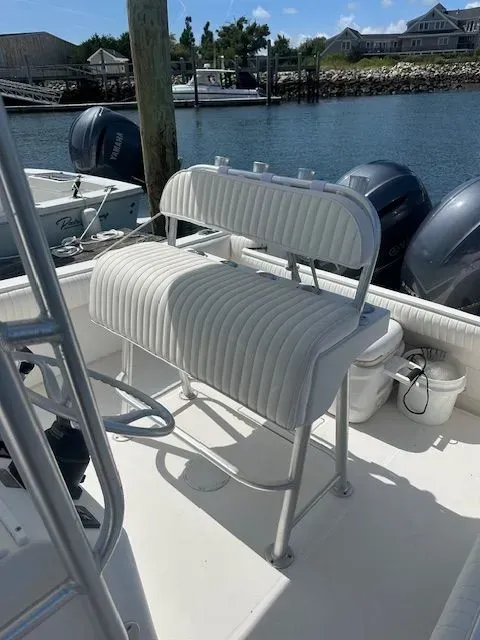 White boat bench seat with backrest, in a boat on the water, with blue engines and dock in background.