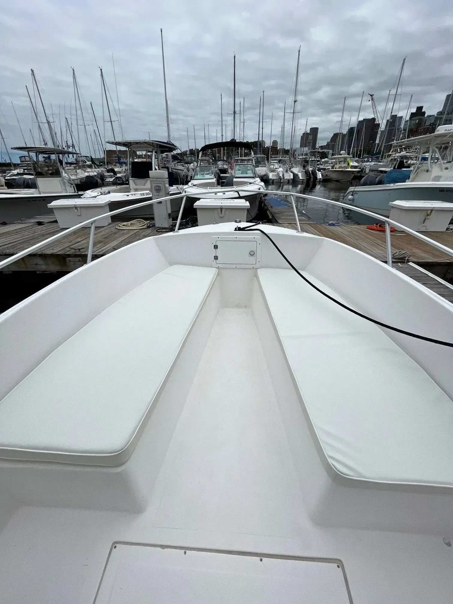 White boat interior with two cushioned benches, docked at a marina on a cloudy day.