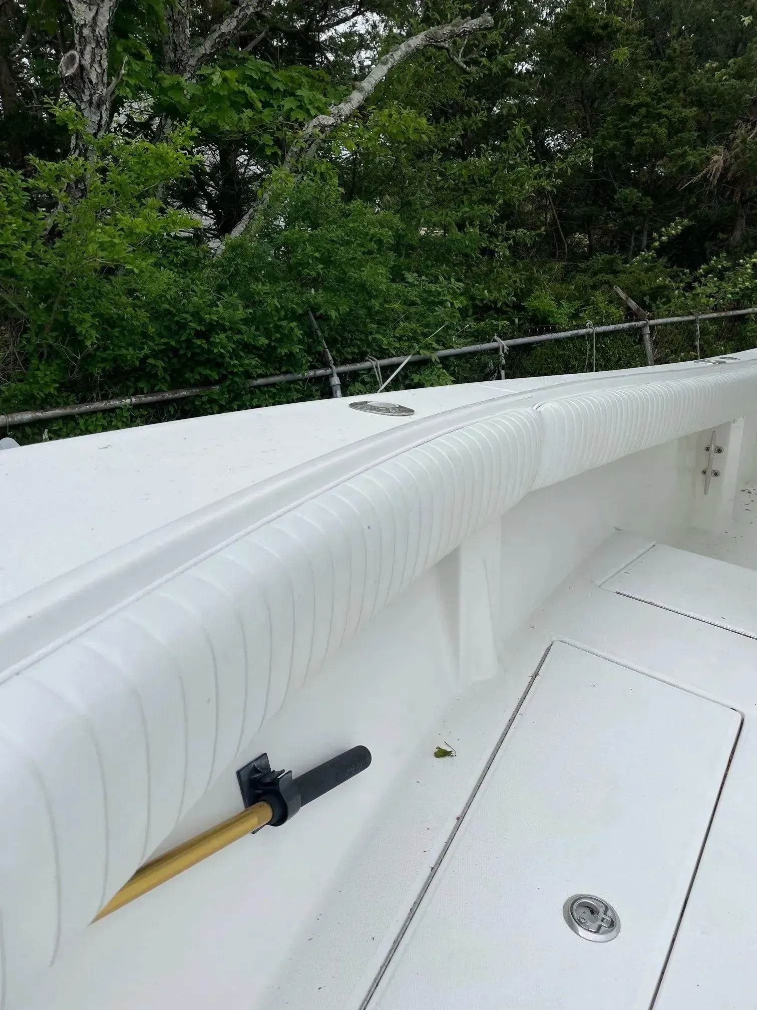 White boat interior with padded bolster and stainless steel railing; trees in background.