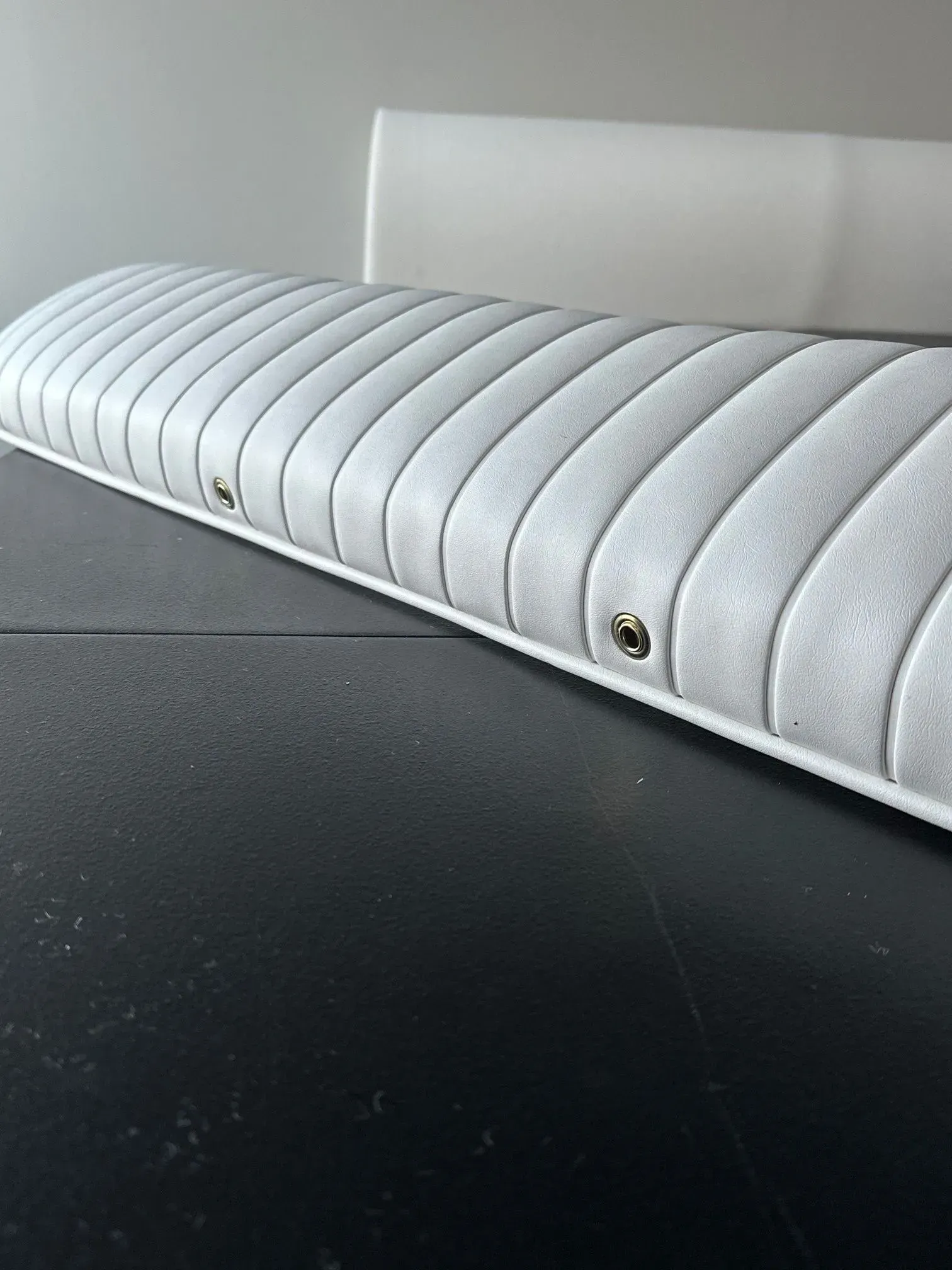 Gray, padded, boat seat with vertical stitching and metal grommets on a dark surface.