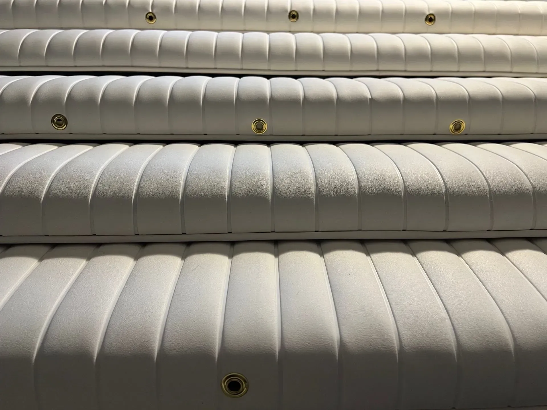 Close-up of several white, vertically ribbed cushions, each with brass-colored grommets.