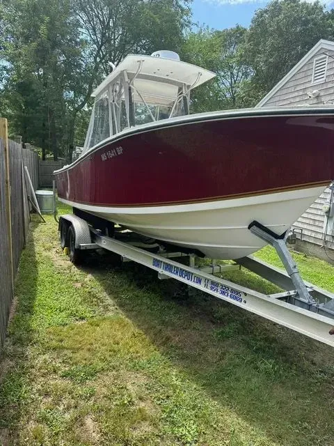 Maroon and white boat on a trailer, parked on grass.