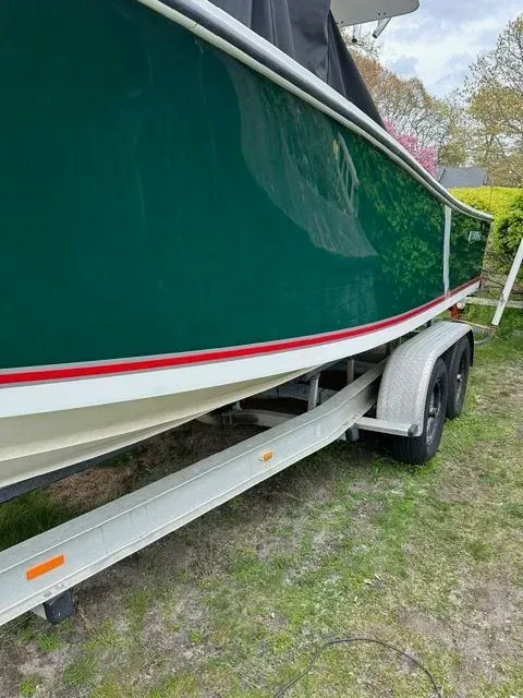 Green boat on a trailer, white and red trim, parked on grass.