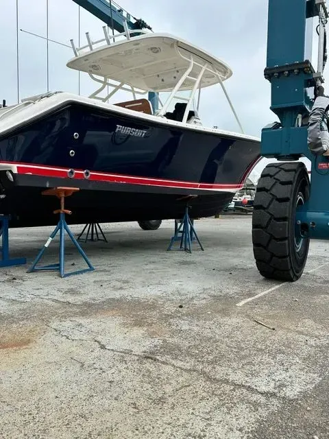 Blue boat on jack stands at a boatyard; a large blue crane wheel is on the right.