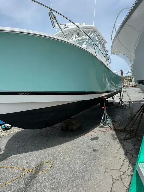 Large teal and white boat on supports in a shipyard.