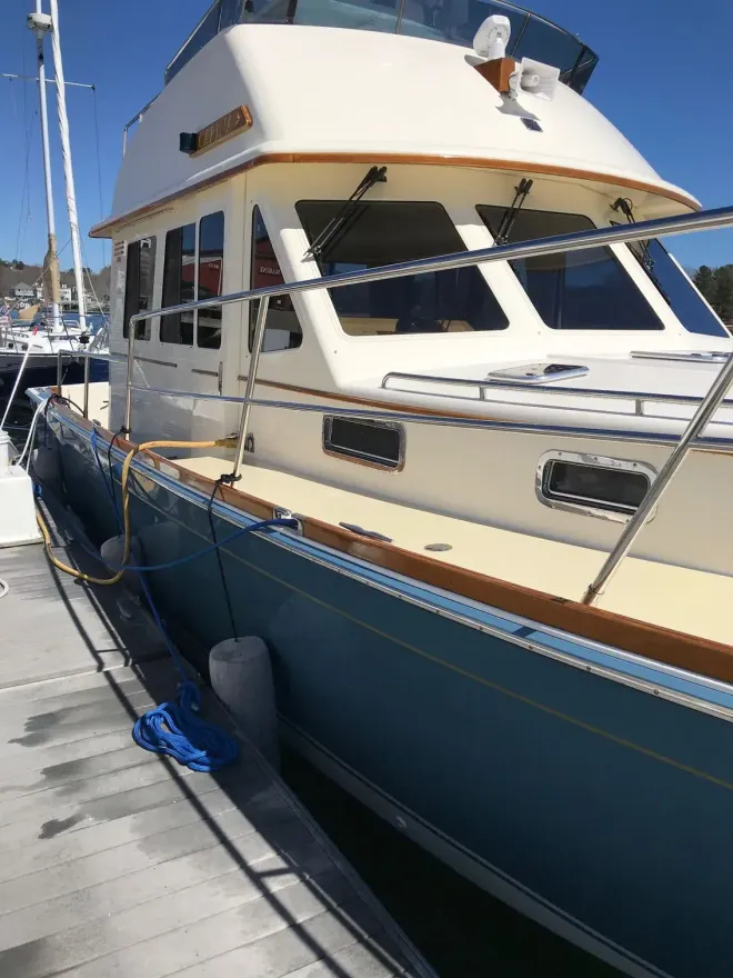 A dark blue boat with a cream-colored windshield frame, propped on metal stands in a storage lot.