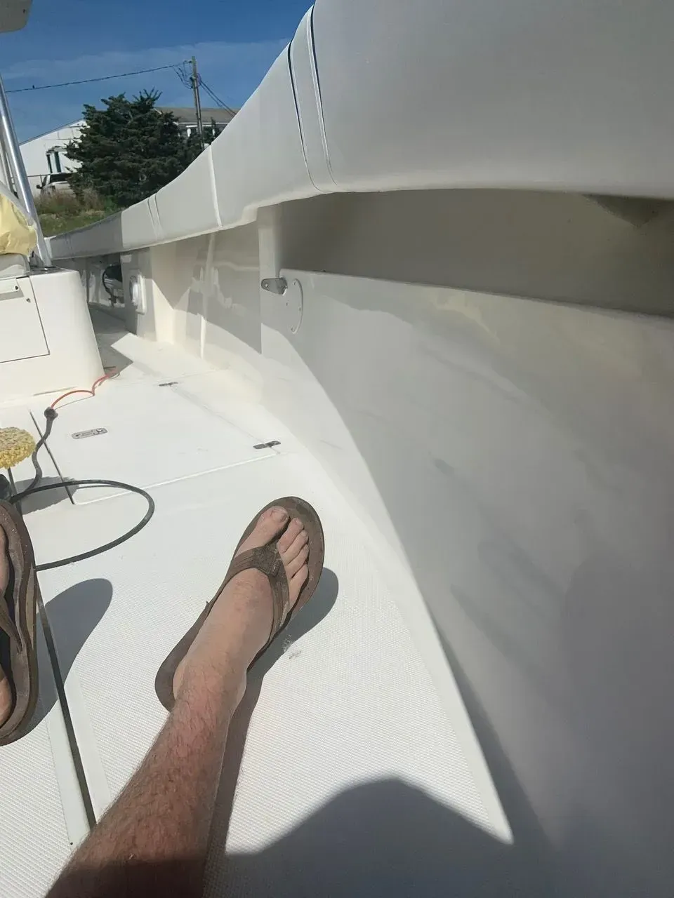 A person wearing flip-flops sits on the deck of a white boat, with a railing running along the side.