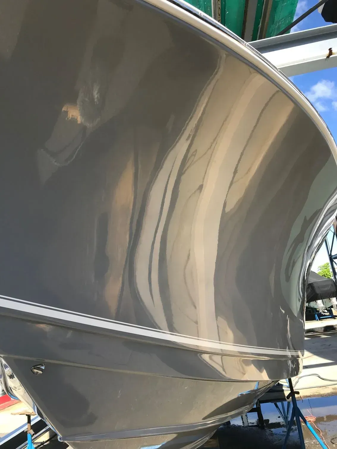 A close-up, low-angle view of the glossy, grey, curved hull of a boat parked in an outdoor storage area.