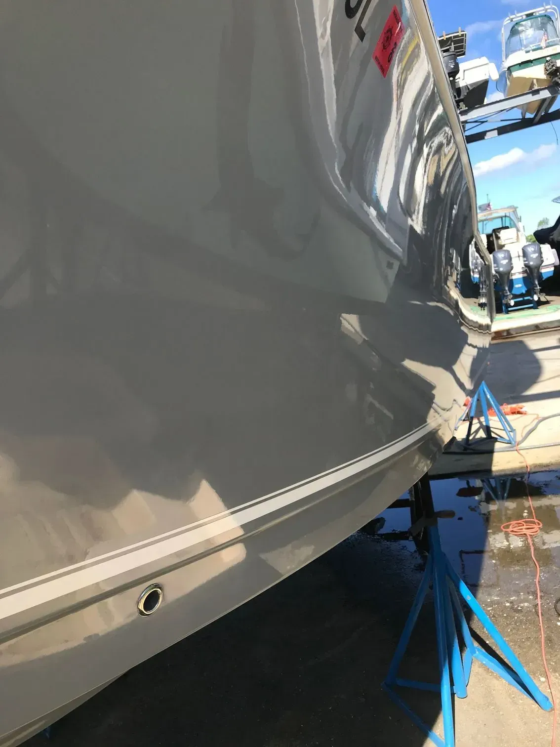 The side hull of a light gray boat resting on blue jack stands at a shipyard.