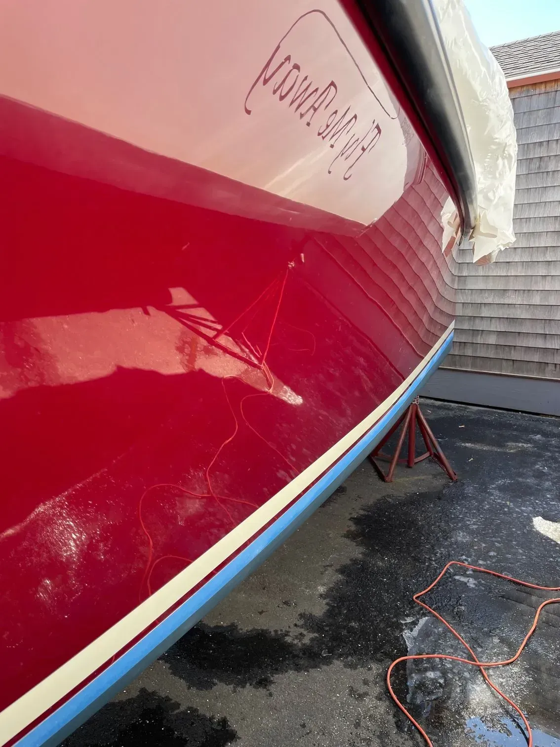 The glossy red hull of a boat sits on a stand, showing a reflected name and a blue stripe along the bottom.