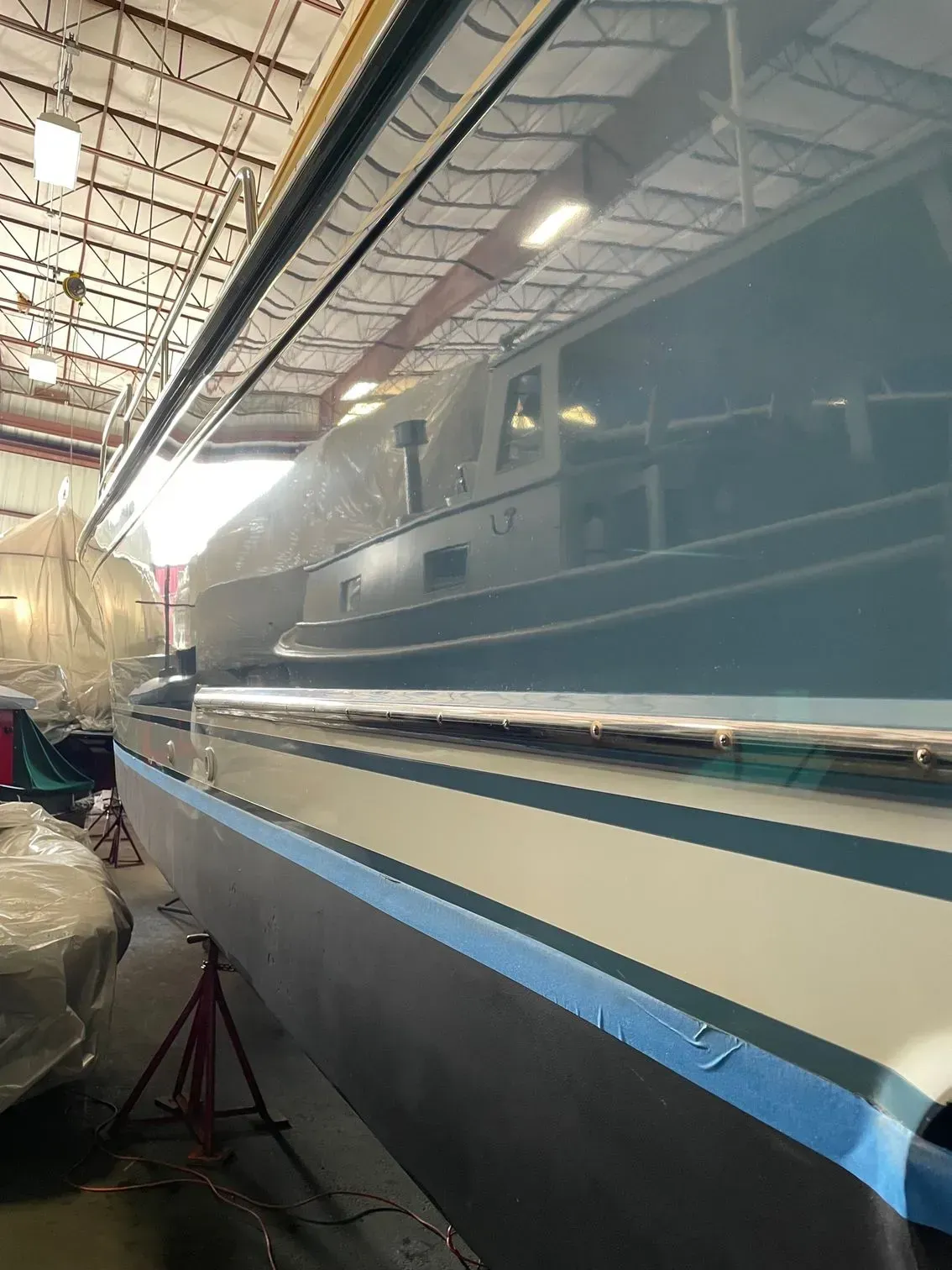 A motorboat with grey, white, and blue stripes sitting on jack stands inside a bright warehouse facility.
