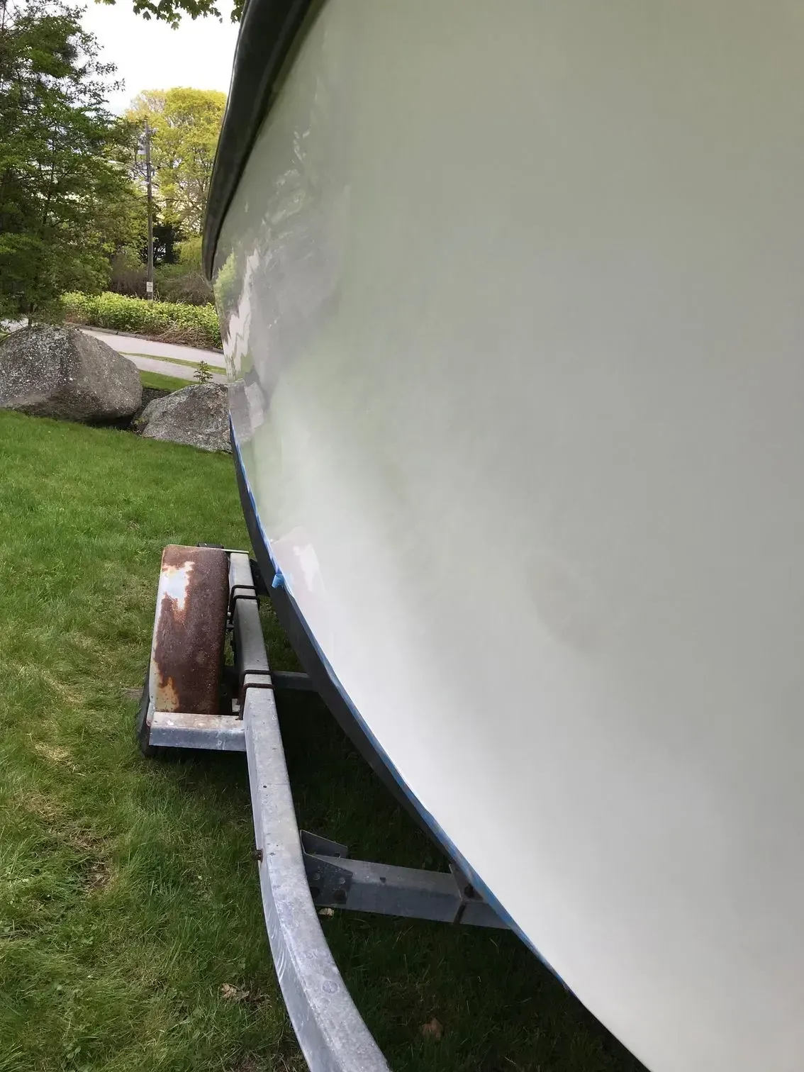 A side view of a light-colored boat hull on a metal trailer in a grassy, outdoor area.