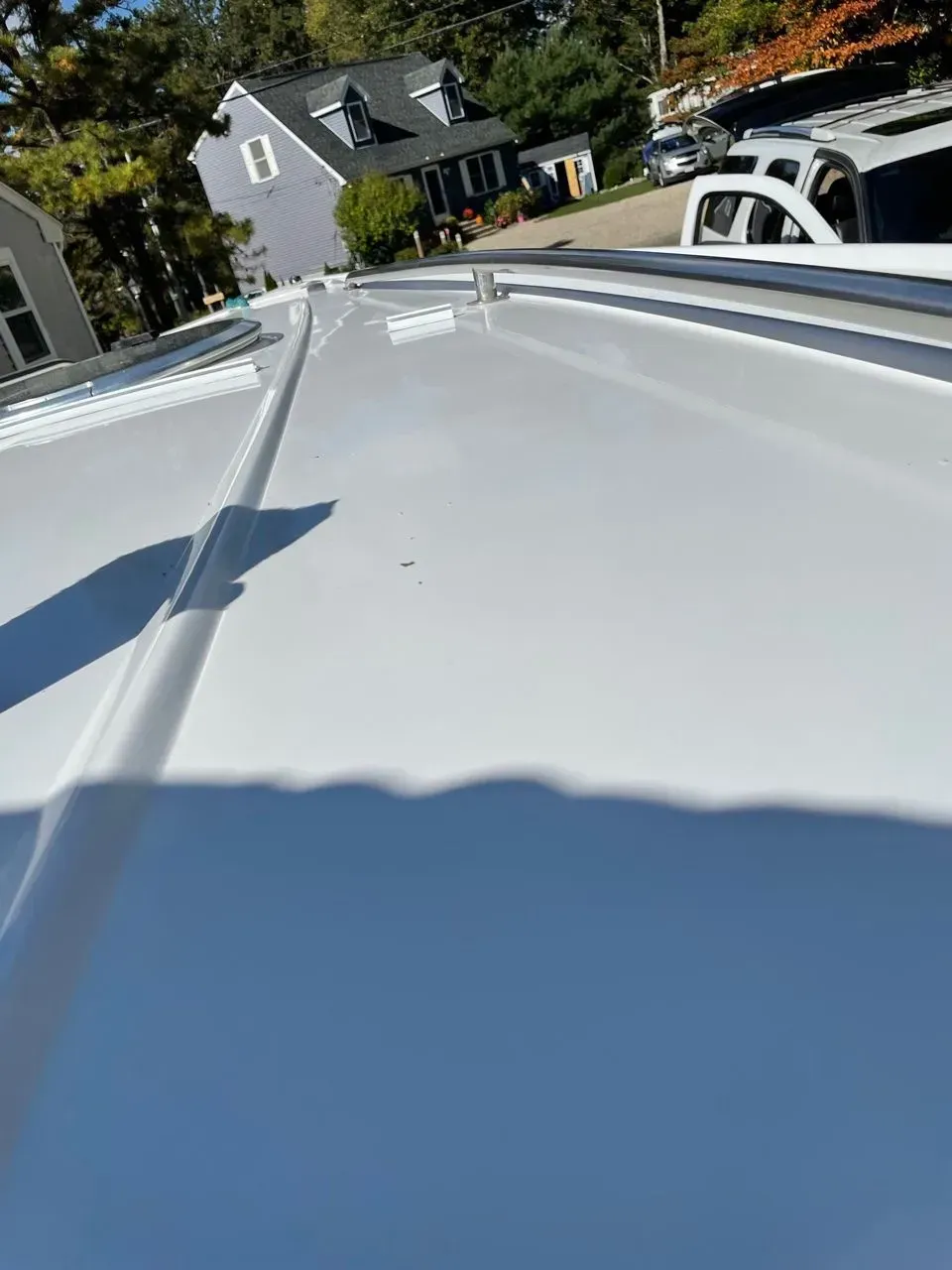 A high-angle view of a white van roof featuring longitudinal ridges and a metal roof rack rail.