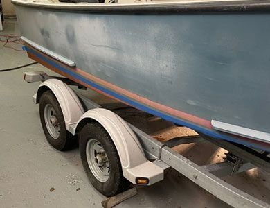A light blue boat sits on a dual-axle metal trailer with white fenders in a garage setting.