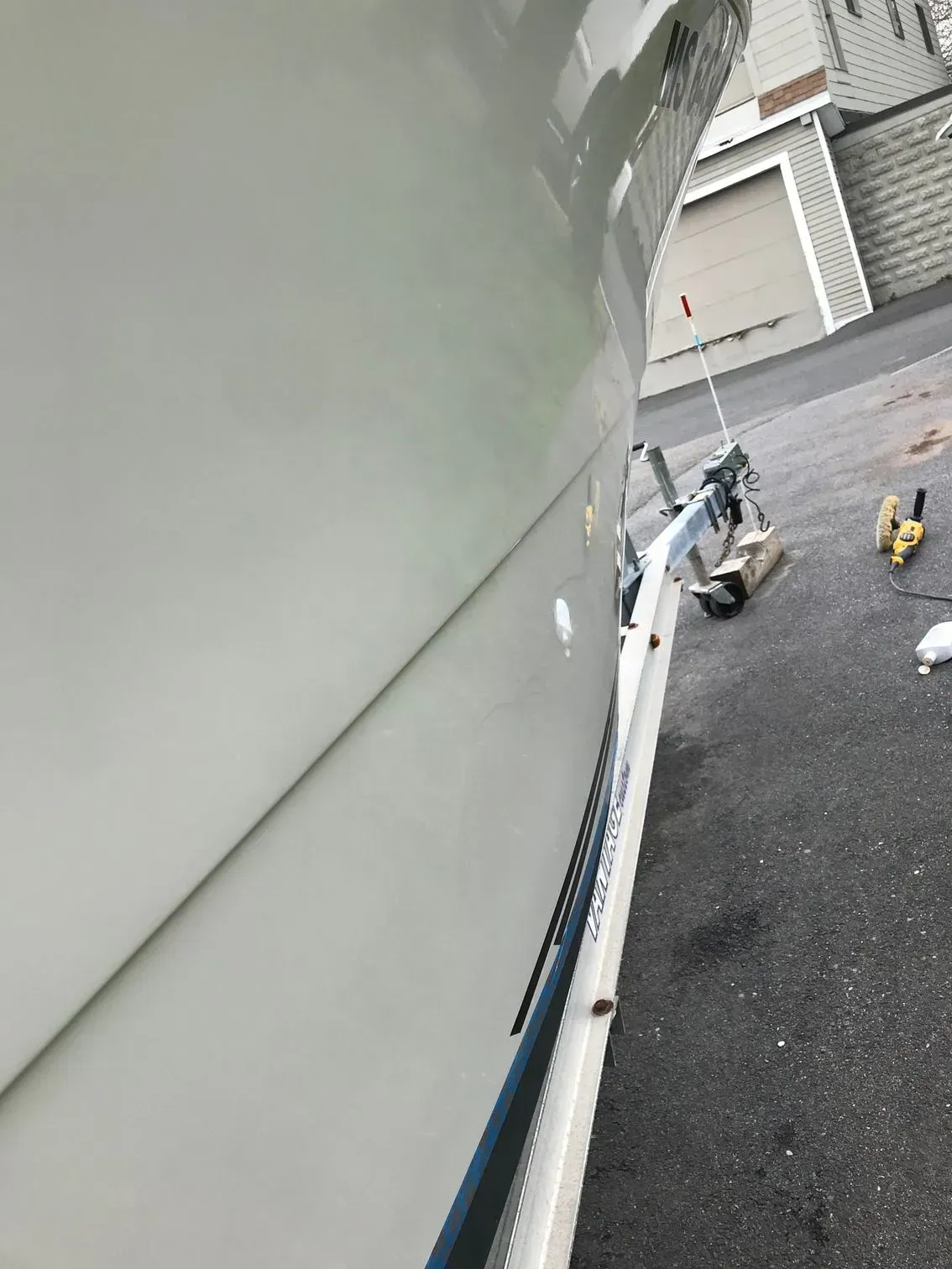 Side view of a white boat hull resting on a trailer parked on asphalt near a building.