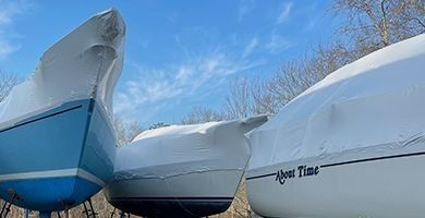 Three boats in storage stands, covered in white shrink wrap under a clear blue sky.
