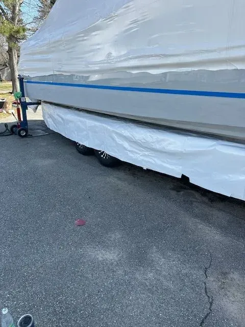 A boat wrapped in white protective plastic sits on a trailer in an outdoor parking area.