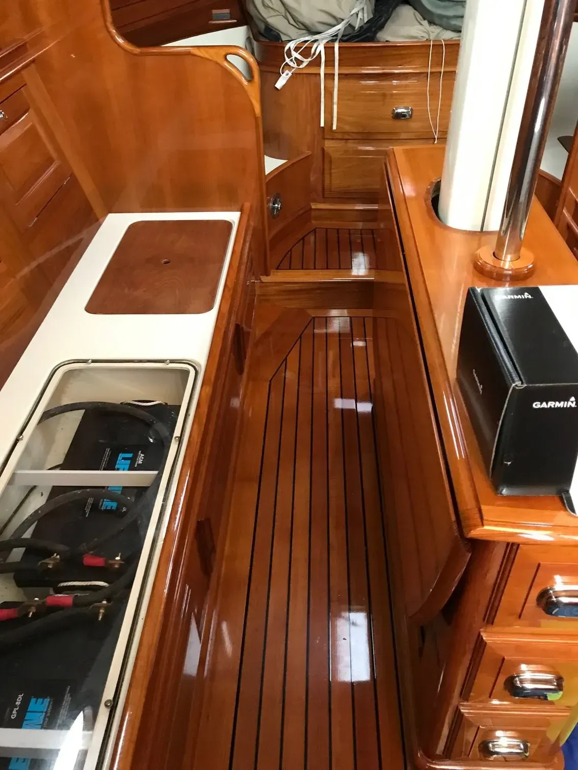 A narrow wooden companionway inside a boat, featuring varnished teak panels, a slatted floor, and a built-in counter.