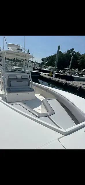 The bow deck of a white center console boat with gray cushioned seating, docked at a marina on a sunny day.