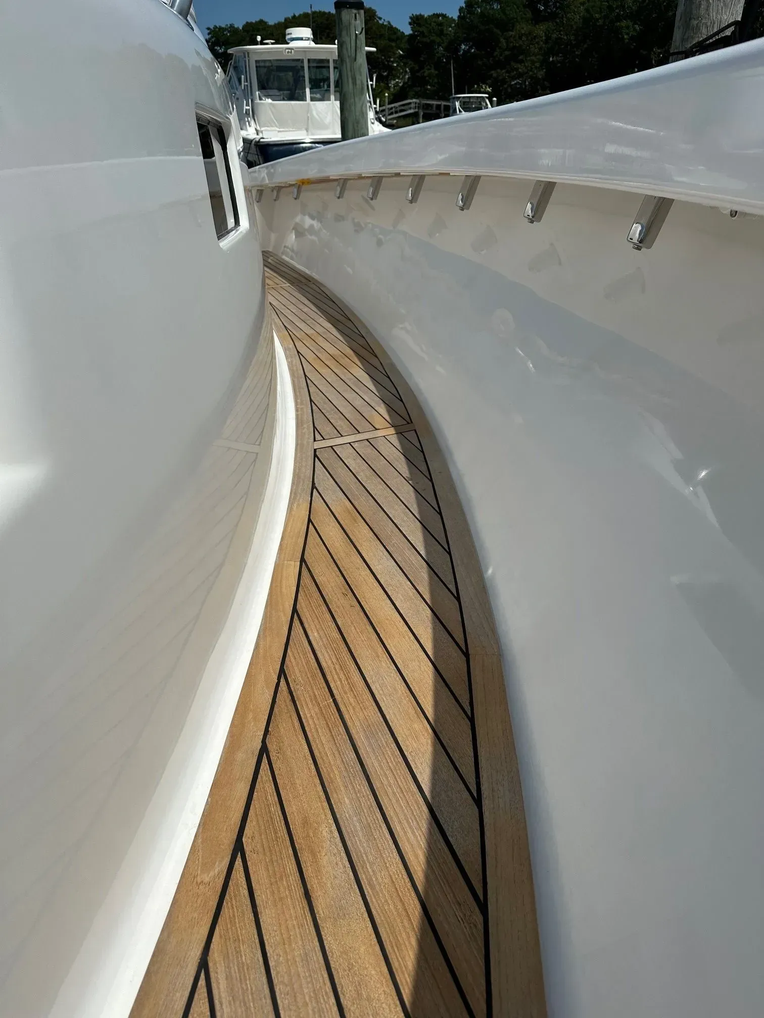 A narrow teak-paneled walkway curves along the side of a white yacht, with smooth, reflective hull walls on either side.