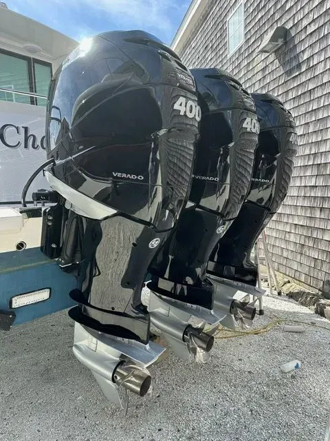 A close-up of three black 400-horsepower outboard boat motors mounted on the back of a boat near a shingled wall.
