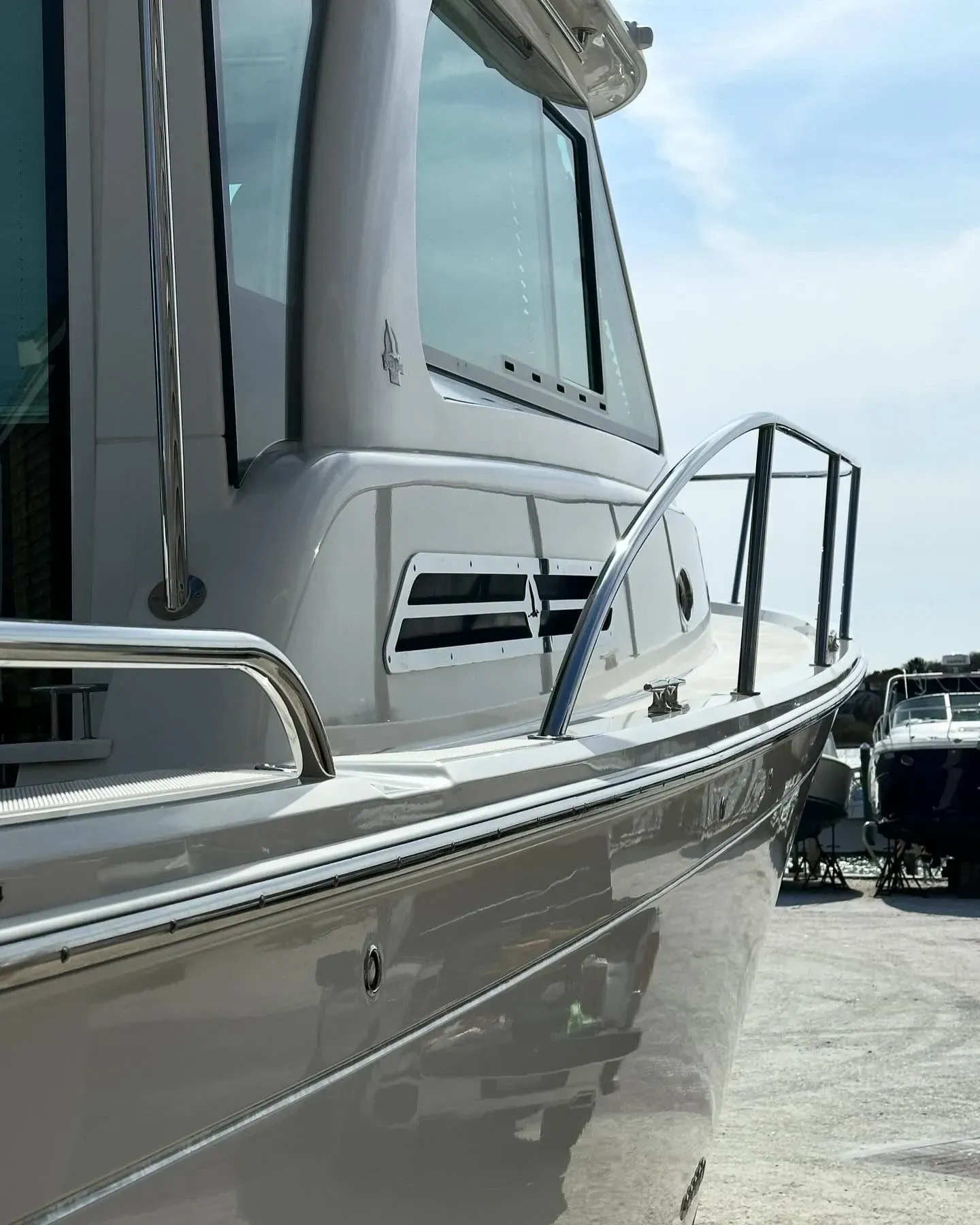 Close-up of a sleek, light-colored boat hull and cabin railing in a shipyard on a sunny day.