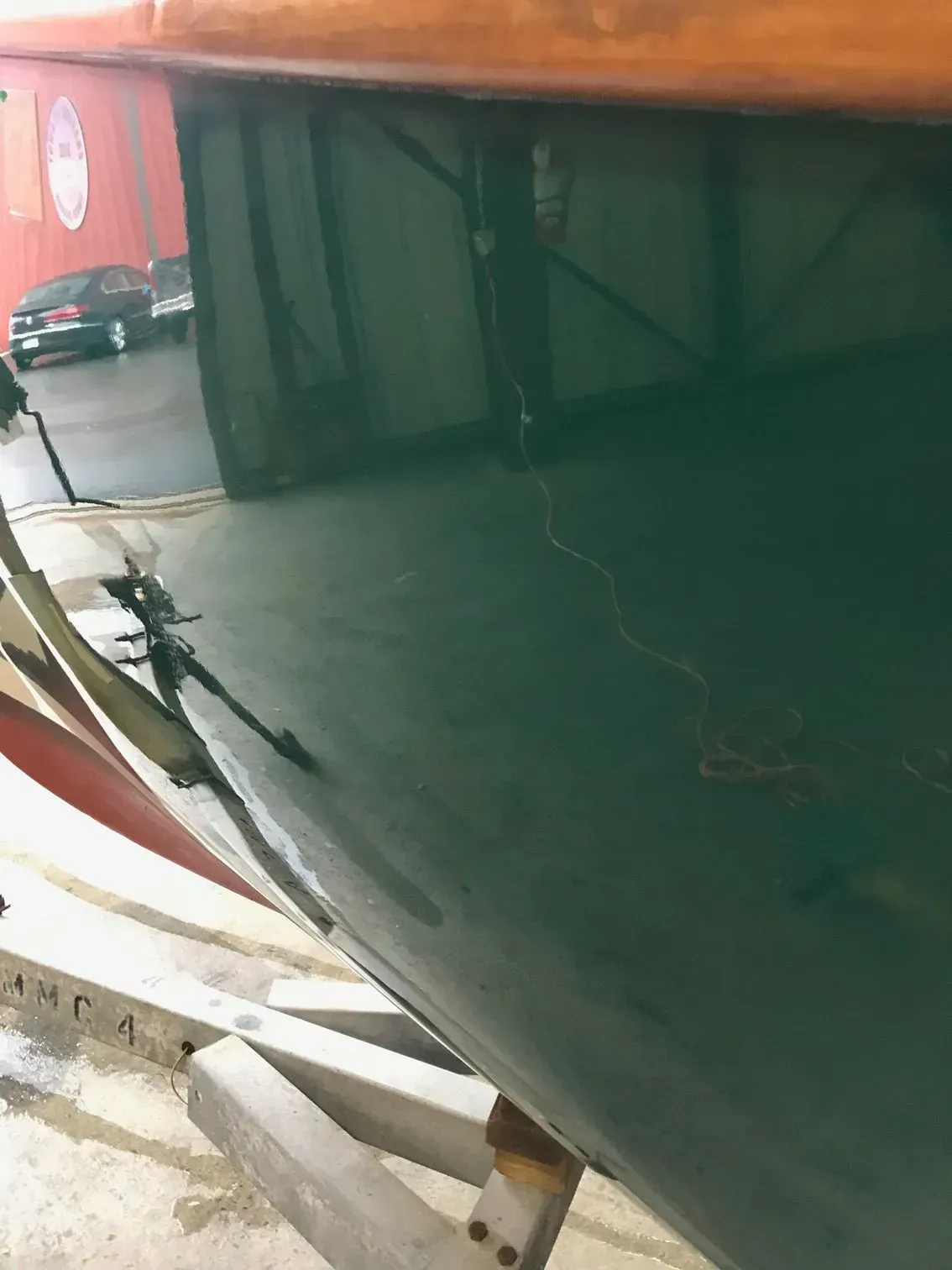 A close-up view of the dark green, reflective hull of a wooden boat sitting on a metal trailer in a parking area.