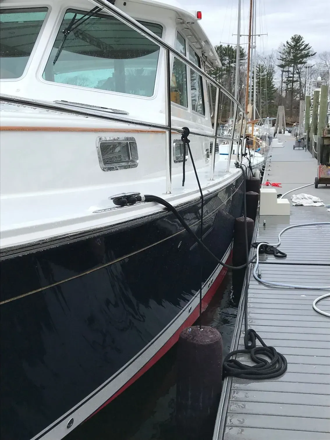 A side view of a navy blue and white yacht moored at a wooden dock.