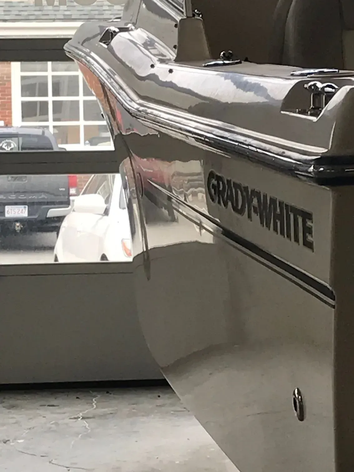 Close-up of a glossy, tan Grady-White boat hull reflecting a car and garage exterior.