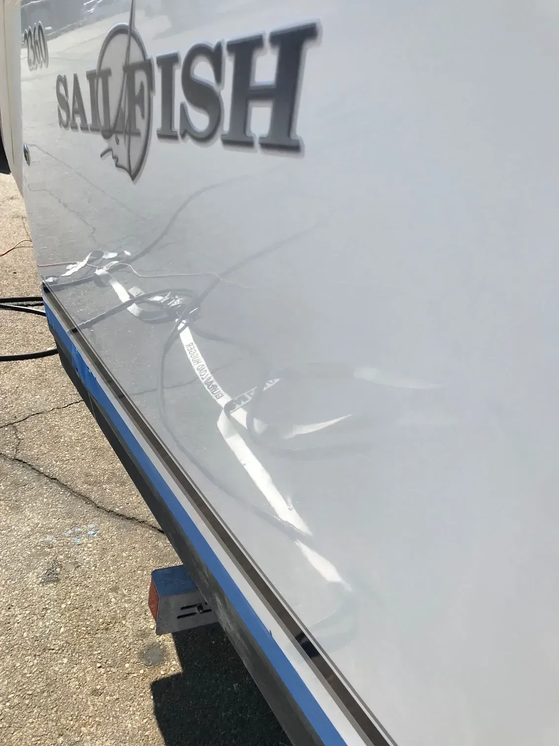 A close-up of a white boat hull with the Sailfish logo, viewed from an angle showing a reflection on the shiny surface.