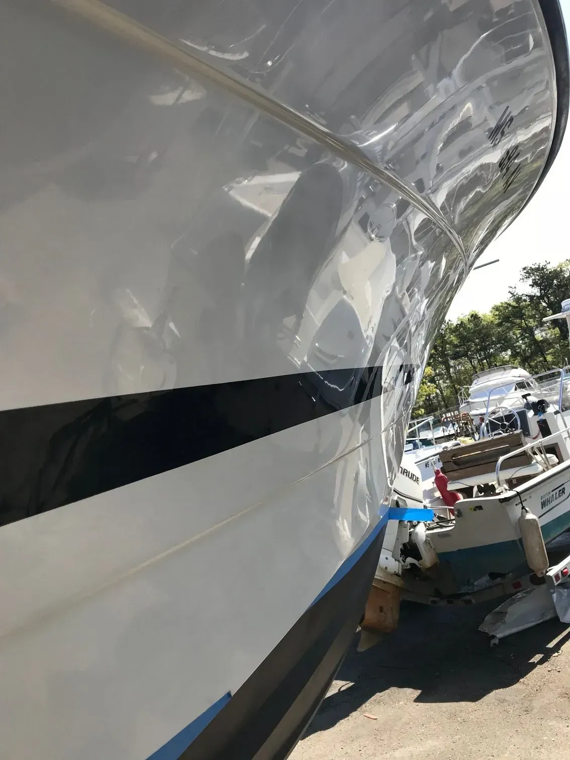 Close-up of a white boat hull with a black stripe, shown angled against a background of other boats on trailers.