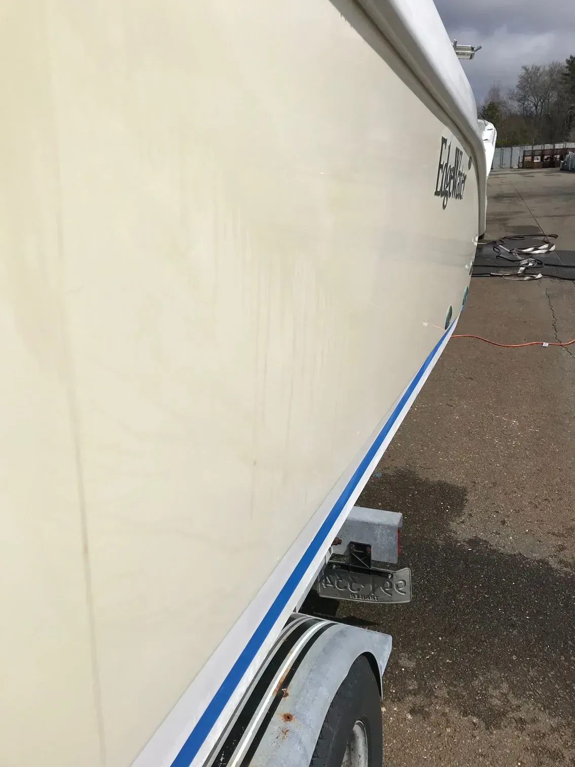 A close-up view of the pale yellow side of a boat hull on a trailer, featuring a thin blue stripe and black lettering.