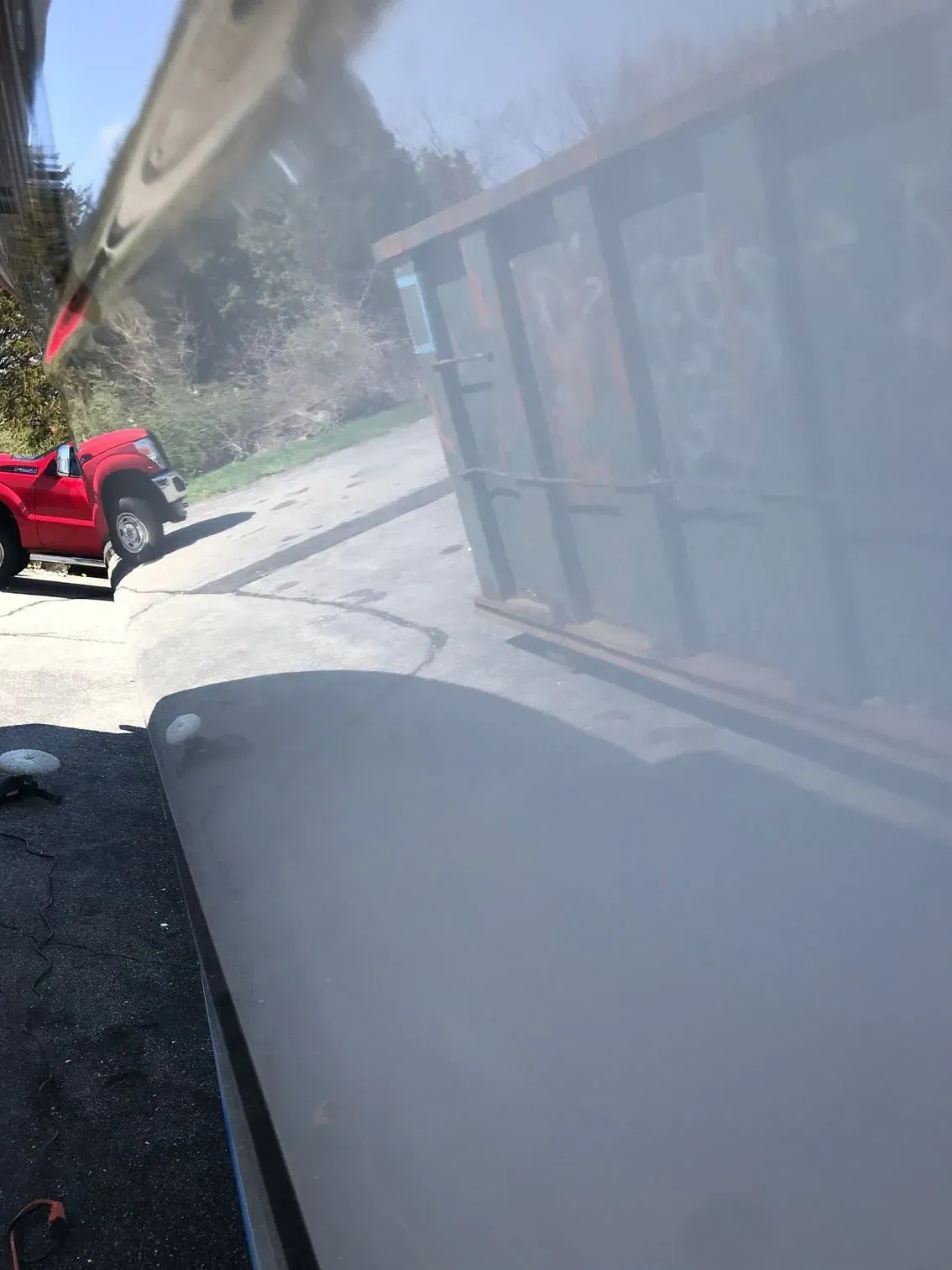 A red pickup truck parked on pavement next to a green structure, viewed through a reflective window.