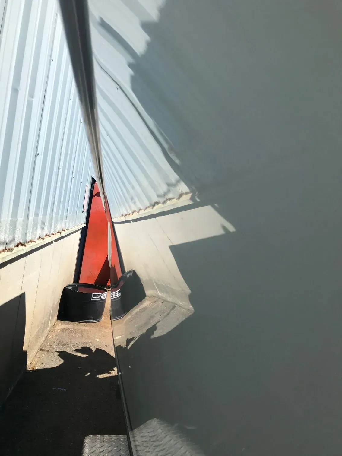 A narrow, sunlit indoor passage with corrugated metal walls and a small orange marker at the end.