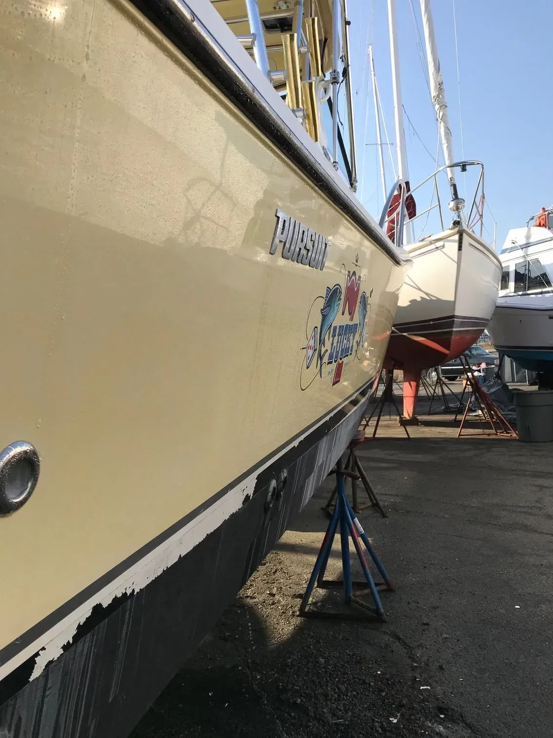 The side view of a cream-colored boat hull with a crab decal, parked on metal stands at a boat yard.