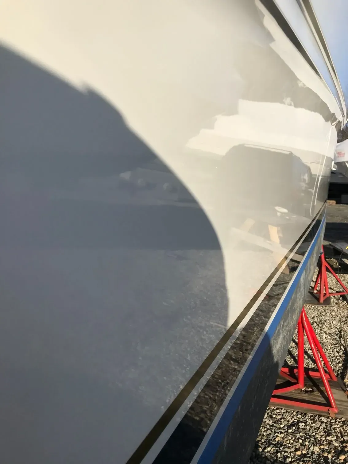 A close-up of a smooth, white boat hull supported by red jack stands on a gravel surface.