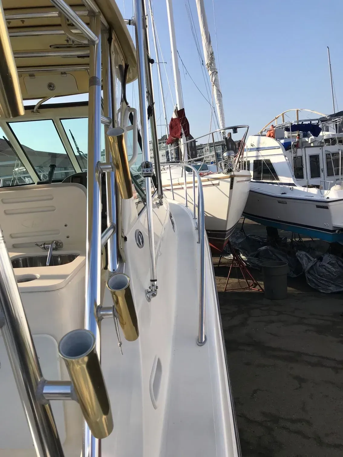 Side view of boat deck with gold rod holders, parked at a boatyard with other docked vessels in the background.