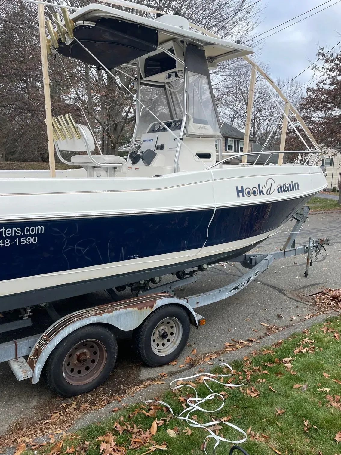 A white and dark blue center console fishing boat on a dual-axle metal trailer parked on pavement near a grassy area.