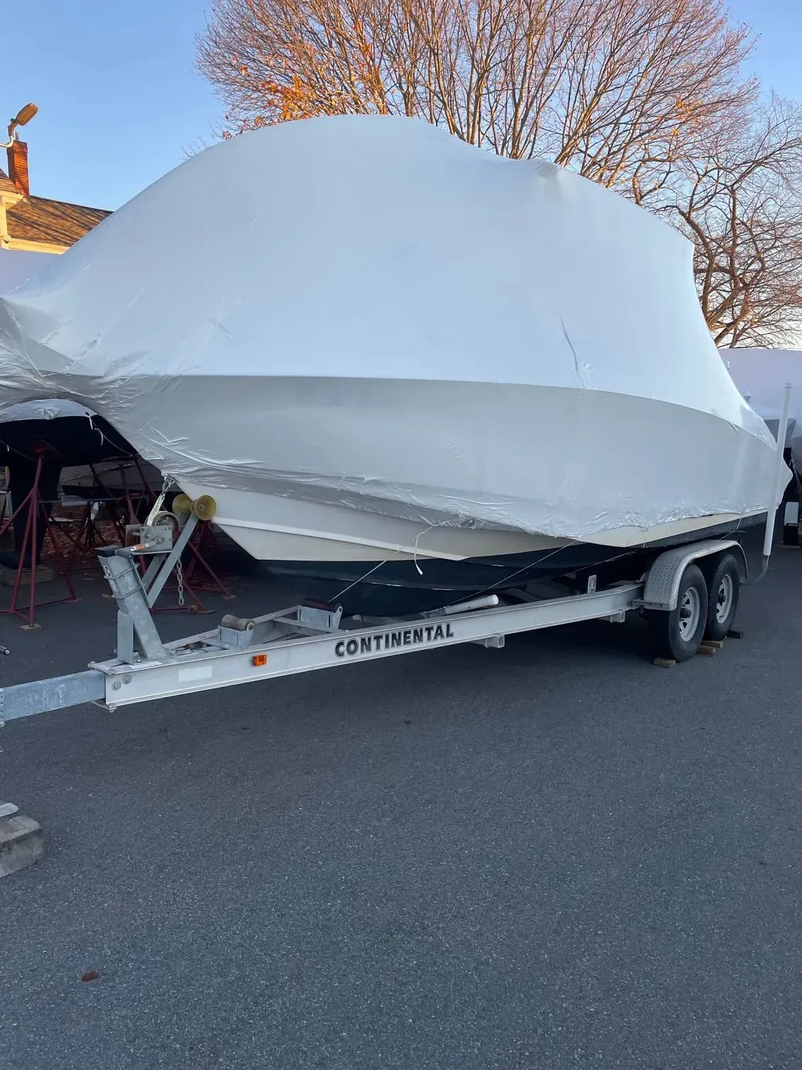 A shrink-wrapped white boat sits on a Continental tandem-axle trailer in a paved lot under a clear blue sky.